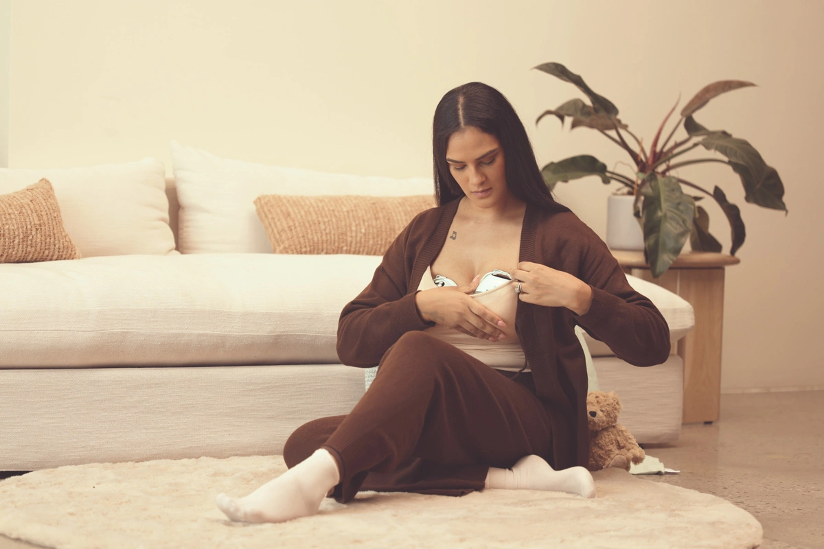 woman using the zomee w1 warming wearable breast pump in a living room